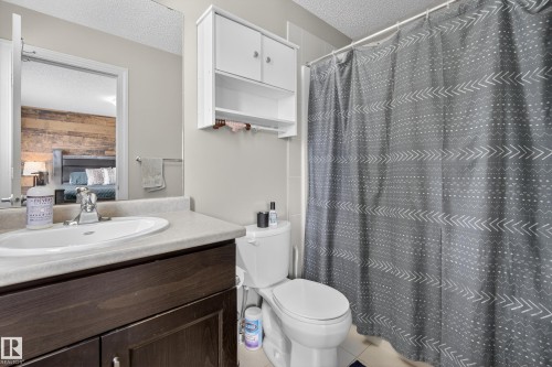 Bathroom featuring a vanity with an integrated sink, dark wood-finish cabinetry, white wall-mounted storage, a toilet, and a tiled shower area - 7074 Cardinal Way, Edmonton, AB - Indoor Photo Showing Bathroom