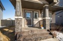 Inviting front entrance featuring a covered porch, stone-clad columns, durable siding, and a wooden fence - 7074 Cardinal Way, Edmonton, AB  - Outdoor With Deck Patio Veranda 