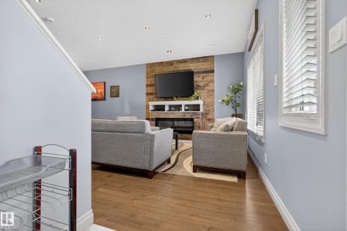 Living area featuring wood-finish flooring, recessed lighting, and a prominent wood-paneled accent wall with a built-in fireplace - 7074 Cardinal Way, Edmonton, AB - Indoor With Fireplace