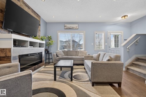 Living area featuring a modern fireplace with a wood-finish accent wall, built-in media shelving, and recessed lighting - 7074 Cardinal Way, Edmonton, AB - Indoor Photo Showing Living Room With Fireplace