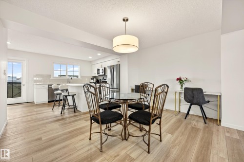 Open-concept kitchen and dining area featuring wood-finish flooring, white cabinetry, stainless steel appliances, and a tiled backsplash - 38 Jensen Gate, St. Albert, AB - Indoor Photo Showing Dining Room