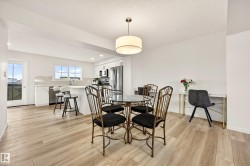 Open-concept kitchen and dining area featuring wood-finish flooring, white cabinetry, stainless steel appliances, and a tiled backsplash - 