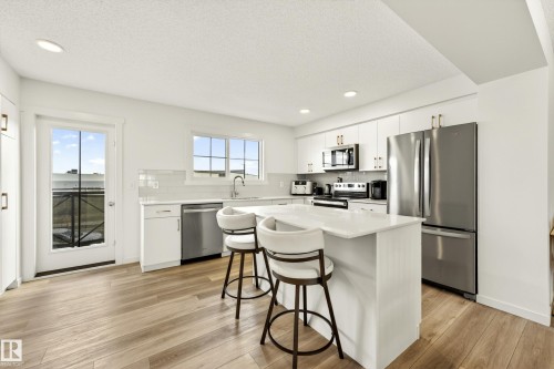 Contemporary kitchen featuring wood-finish flooring, white cabinetry, integrated stainless steel appliances, a center island with countertop seating, and recessed lighting - 38 Jensen Gate, St. Albert, AB - Indoor Photo Showing Kitchen With Upgraded Kitchen