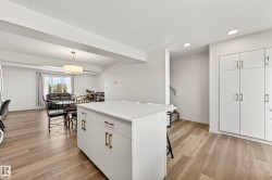 Open-concept living space featuring wood-finish flooring, a kitchen island with storage and seating, and extensive white cabinetry - 