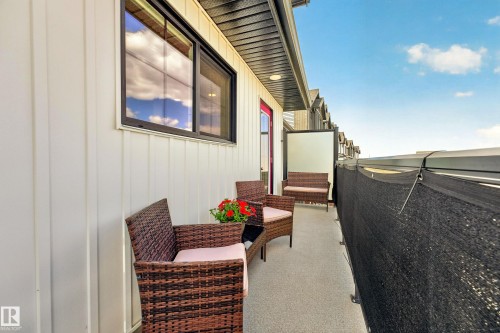 Exterior balcony featuring white vertical siding, a dark-framed sliding window, a red entry door, a gray concrete-finish surface, and a black privacy screen - 38 Jensen Gate, St. Albert, AB -  With Exterior