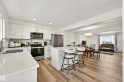 Kitchen featuring wood-finish flooring, white cabinetry with gold-tone hardware, stainless steel appliances, and white countertops - 