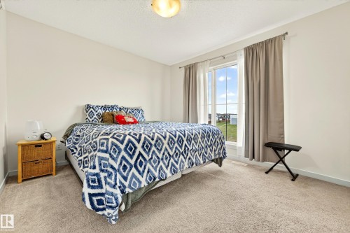 Carpeted bedroom featuring neutral wall tones, a large window with white trim, and a ceiling-mounted light fixture - 38 Jensen Gate, St. Albert, AB - Indoor Photo Showing Bedroom