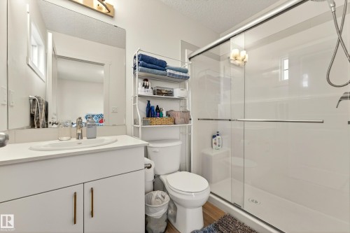Bathroom featuring a single vanity with an integrated sink, a large wall-mounted mirror, a toilet, a glass-enclosed shower, and wood-finish flooring - 38 Jensen Gate, St. Albert, AB - Indoor Photo Showing Bathroom