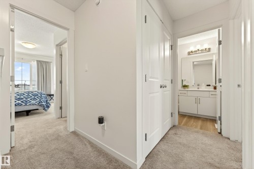 Carpeted hallway with white walls and trim, featuring a bedroom with a large window and a bathroom with a vanity and mirror - 38 Jensen Gate, St. Albert, AB - Indoor Photo Showing Other Room