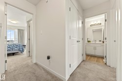 Carpeted hallway with white walls and trim, featuring a bedroom with a large window and a bathroom with a vanity and mirror - 