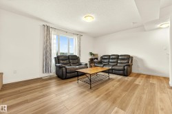 Spacious living area featuring large windows with natural light, wood-finish flooring, and neutral white walls - 