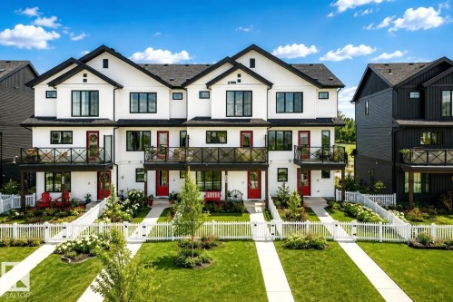 Modern farmhouse-inspired townhomes featuring white siding with black trim, individual balconies, and red entry doors - 38 Jensen Gate, St. Albert, AB - Outdoor With Balcony With Facade