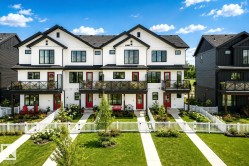 Modern farmhouse-inspired townhomes featuring white siding with black trim, individual balconies, and red entry doors - 