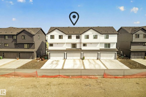 Modern townhome exterior featuring white siding with black trim, dark shingle roofing, and three individual garage bays with concrete driveways - 38 Jensen Gate, St. Albert, AB - Outdoor With Facade
