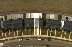 Aerial view showcasing a residential street with multiple properties, each featuring a dark-toned roof and light-toned front yard paths - 