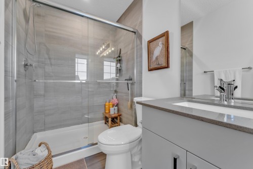 Contemporary bathroom featuring a spacious glass-enclosed shower with gray tiled walls and a polished chrome shower head, a large vanity with a rectangular undermount sink, a gray countertop, and a chrome faucet, and wood-finish flooring - 17319 2 St Nw, Edmonton, AB - Indoor Photo Showing Bathroom