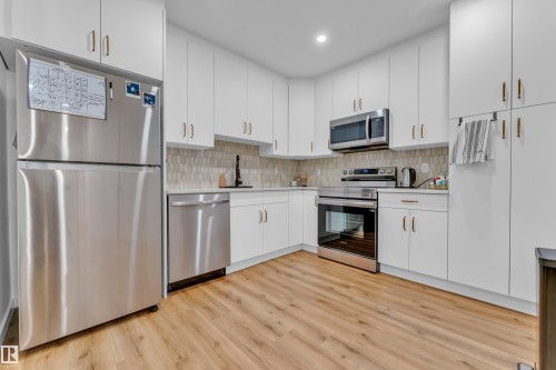 Modern kitchen featuring white cabinetry, stainless steel appliances, a unique patterned backsplash, light wood-finish flooring, and ample storage - 17319 2 St Nw, Edmonton, AB - Indoor Photo Showing Kitchen With Stainless Steel Kitchen