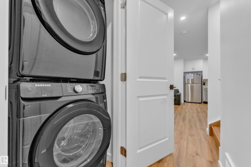 Stacked laundry appliances with a modern dark finish, recessed lighting, wood-finish flooring, and white interior doors - 17319 2 St Nw, Edmonton, AB - Indoor Photo Showing Laundry Room