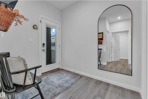 Entryway featuring light gray walls, wood-finish flooring, and a contemporary arched mirror - 17319 2 St Nw, Edmonton, AB - Indoor Photo Showing Other Room