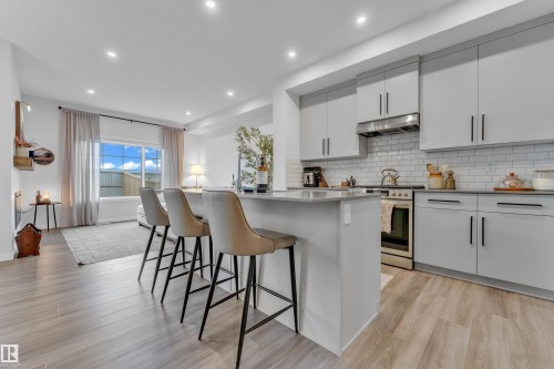 Contemporary kitchen featuring light gray cabinetry, stainless steel appliances, a subway tile backsplash, and a central island with a solid surface countertop - 17319 2 St Nw, Edmonton, AB - Indoor Photo Showing Kitchen With Upgraded Kitchen