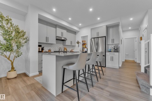Modern kitchen featuring wood-finish flooring, recessed lighting, light gray cabinetry, stainless steel appliances, and a central island with bar seating - 17319 2 St Nw, Edmonton, AB - Indoor Photo Showing Kitchen With Stainless Steel Kitchen With Upgraded Kitchen