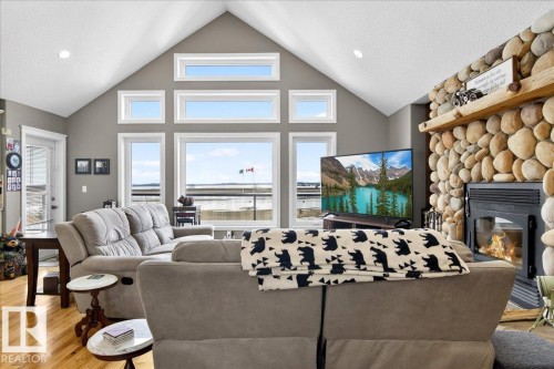 This living space features prominent windows, a stone-clad fireplace with a timber mantel, and light-toned hardwood flooring - 531064 Range Road 174, Rural Lamont County, AB - Indoor Photo Showing Living Room With Fireplace