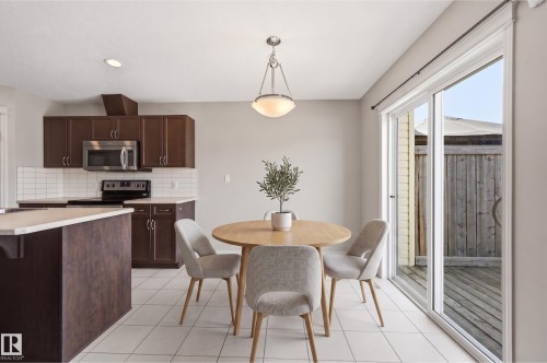 Kitchen and dining area featuring a sliding glass door to an exterior deck, white tile flooring, dark wood cabinetry, stainless steel appliances, and a tiled backsplash - 2170 52A Street Sw, Edmonton, AB - Indoor