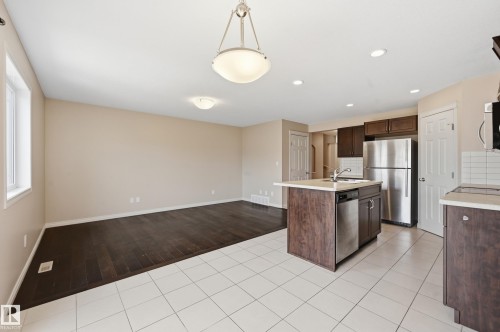 Open-concept living space featuring wood-finish flooring, a kitchen island with integrated sink, stainless steel appliances, and white tile flooring - 2170 52A Street Sw, Edmonton, AB - Indoor Photo Showing Kitchen