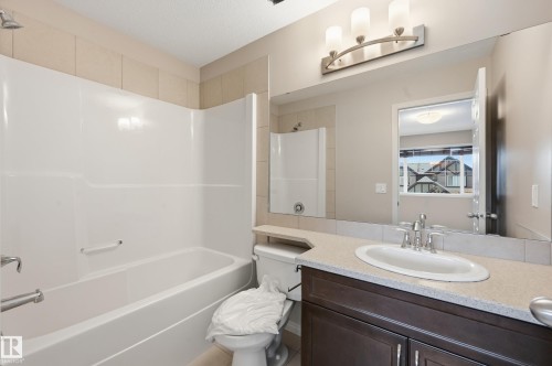 Bathroom featuring a white shower-tub combination, a dark wood-finish vanity with ample storage, a light-toned countertop, a white oval undermount sink, and a large mirror with a three-light fixture - 2170 52A Street Sw, Edmonton, AB - Indoor Photo Showing Bathroom