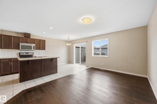 Open-concept living area featuring rich wood-finish flooring, a kitchen island with seating, stainless steel appliances, and a white subway tile backsplash - 2170 52A Street Sw, Edmonton, AB - Indoor Photo Showing Kitchen