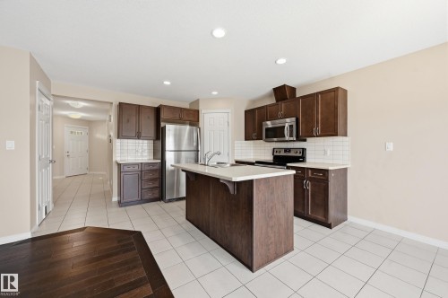 Kitchen featuring dark wood-finish cabinetry, stainless steel appliances, a center island with light-toned countertop, and white subway tile backsplash - 2170 52A Street Sw, Edmonton, AB - Indoor Photo Showing Kitchen With Stainless Steel Kitchen
