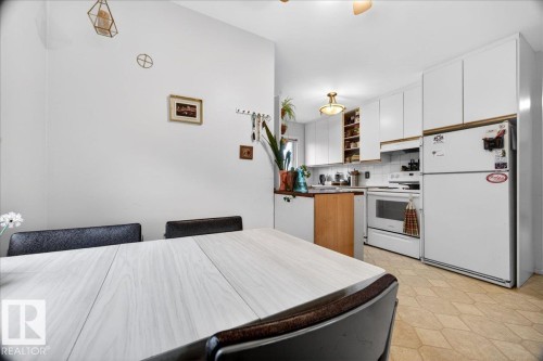 Dining area with a light wood-finish table and dark chairs, opening to a kitchen featuring white cabinetry, white appliances, and a tiled backsplash - 4212 105 Avenue, Edmonton, AB - Indoor Photo Showing Kitchen
