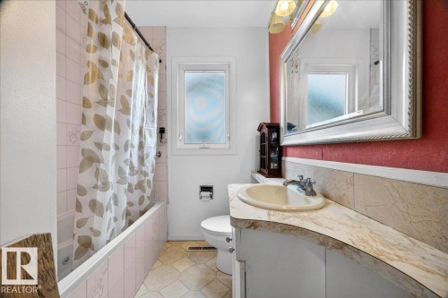 Full bathroom featuring a single vanity with an integrated sink, a large framed mirror with overhead lighting, and a bathtub with pink tiled surround - 4212 105 Avenue, Edmonton, AB - Indoor Photo Showing Bathroom