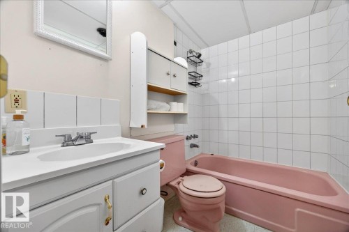Bathroom featuring a white vanity with integrated sink, white tiled backsplash, pink bathtub, and pink toilet - 4212 105 Avenue, Edmonton, AB - Indoor Photo Showing Bathroom