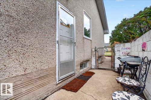 Rear exterior entry featuring a storm door, window, and concrete patio - 4212 105 Avenue, Edmonton, AB - Outdoor With Exterior