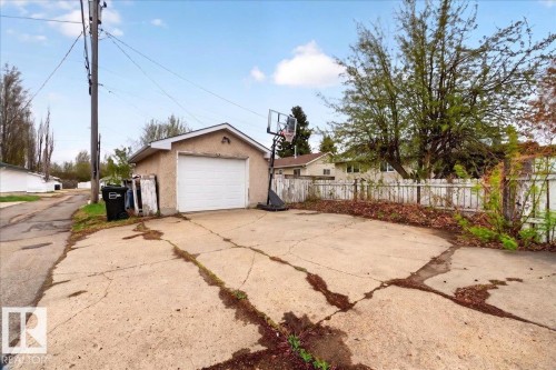 Detached single-car garage featuring a white overhead door and stucco exterior, set on a concrete pad with a partial wooden fence - 4212 105 Avenue, Edmonton, AB - Outdoor
