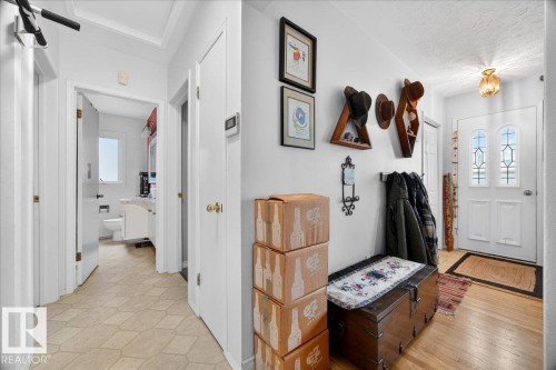 Entryway featuring a decorative front door with arched glass inserts, light wood-finish flooring, white trim, and a hallway leading to an interior room with a window and vanity - 4212 105 Avenue, Edmonton, AB - Indoor Photo Showing Other Room