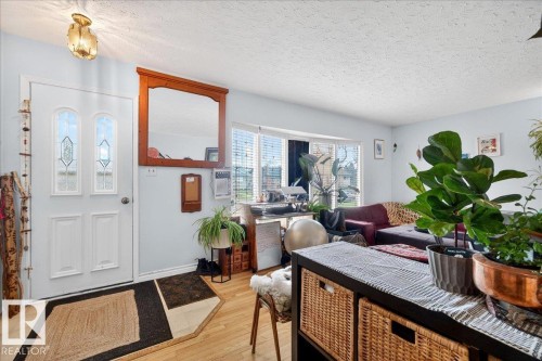 Entryway featuring a white paneled door with decorative glass inserts, wood-finish flooring, a wall-mounted light fixture, and a large bay window - 4212 105 Avenue, Edmonton, AB - Indoor