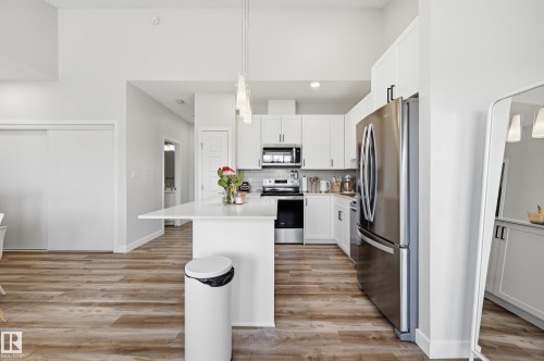 Open-concept kitchen featuring an island with a light-toned countertop, white cabinetry with dark hardware, stainless steel appliances, and wood-finish flooring - 34 2905 141 Street, Edmonton, AB - Indoor Photo Showing Kitchen With Upgraded Kitchen