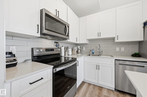 Kitchen featuring white shaker-style cabinetry, light-toned countertops, a subway tile backsplash, and stainless steel appliances including a range, microwave, and dishwasher - 34 2905 141 Street, Edmonton, AB - Indoor Photo Showing Kitchen With Double Sink With Upgraded Kitchen