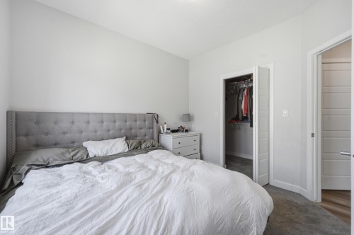 Bedroom featuring light gray wall paint, gray carpet flooring, a walk-in closet with bifold doors, and a paneled interior door with a chrome handle - 34 2905 141 Street, Edmonton, AB - Indoor Photo Showing Bedroom