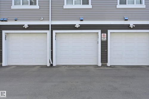Exterior building featuring horizontal siding in a two-tone gray finish, white-framed windows, and three white paneled garage doors - 34 2905 141 Street, Edmonton, AB -  With Exterior