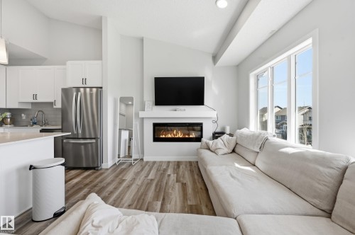 Open-concept living space with wood-finish flooring, a contemporary fireplace, and large windows - 34 2905 141 Street, Edmonton, AB - Indoor Photo Showing Other Room With Fireplace