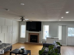 Living area featuring wood-finish flooring, a ceiling fan with light fixture, recessed lighting, and a fireplace with a tile hearth and mantel - 