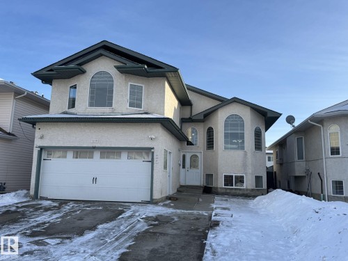 Stucco exterior featuring an arched window, a double garage with decorative hardware, and a white paneled entry door - 3139 34B Avenue, Edmonton, AB 