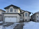 Stucco exterior featuring an arched window, a double garage with decorative hardware, and a white paneled entry door - 3139 34B Avenue, Edmonton, AB 