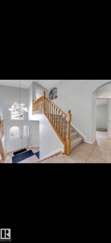 Two-story foyer featuring a grand staircase with wood railings, carpeted treads, and tiled flooring - 3139 34B Avenue, Edmonton, AB 