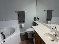 Bathroom featuring a built-in tub with white tile surround, a vanity with an integrated sink and light-toned countertop, a large wall-mounted mirror, and a toilet - 