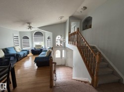 Foyer and living area featuring a decorative chandelier, arched window accents, wood-finish flooring, a ceiling fan, and a wood banister staircase with carpeted steps - 