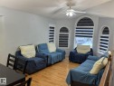 Vaulted ceiling living area featuring multiple arched windows with layered blinds, light wood-finish flooring, and a ceiling fan with integrated lighting - 3139 34B Avenue, Edmonton, AB 